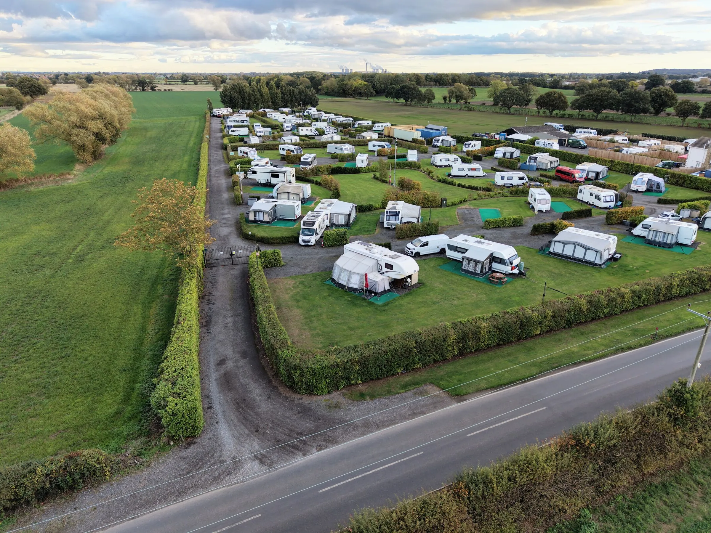 The site from the air, with hedged pitches beside the lane and open countryside beyond